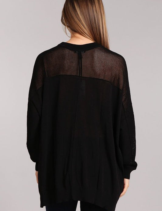 Back view of a black oversized sweater with a fishnet inset and hi-low hemline, showcasing its trendy design.