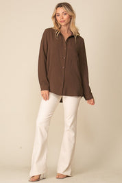 Woman wearing Brooklyn Long Sleeve Blouse, oversized brown button-down with collar, paired with white pants, showcasing relaxed style.