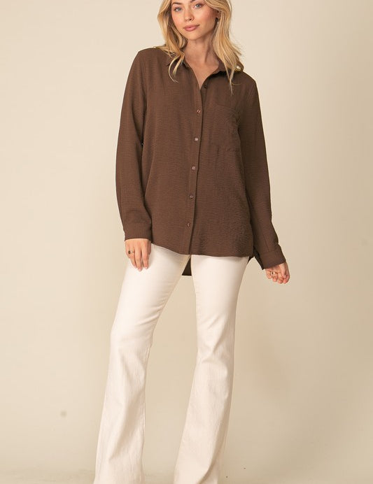 Woman wearing Brooklyn Long Sleeve Blouse, oversized brown button-down with collar, paired with white pants, showcasing relaxed style.