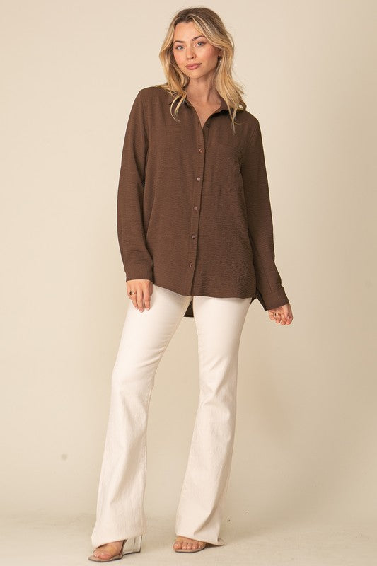 Woman wearing Brooklyn Long Sleeve Blouse, oversized brown button-down with collar, paired with white pants, showcasing relaxed style.