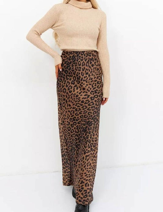 Woman wearing Livia Leopard Satin Skirt with a beige sweater and black boots, showcasing its flowing silhouette and bold print.