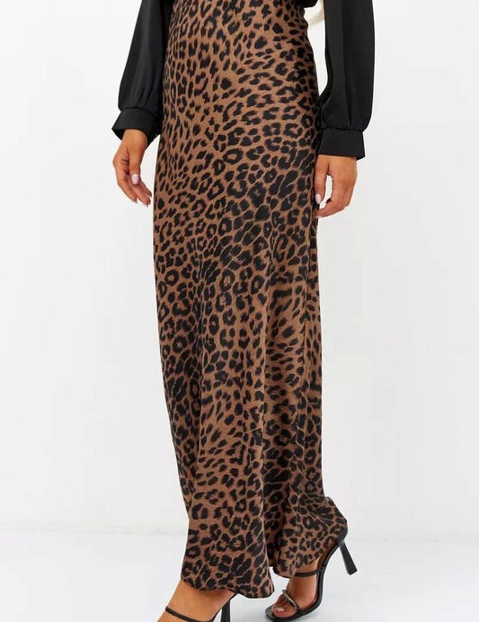 Woman wearing the Livia Leopard Satin Skirt, a long leopard-print skirt crafted from stretchy satin, paired with a black top and heels.