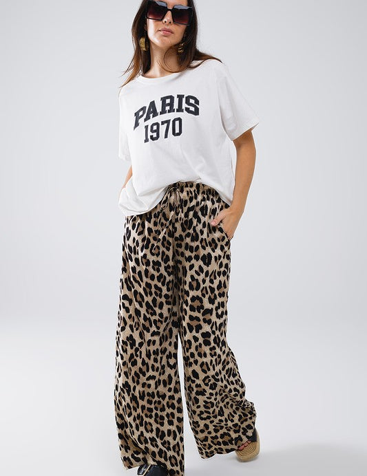 Model wearing Savanna Satin Pants in leopard print with a white Paris t-shirt and sunglasses for a stylish summer outfit.