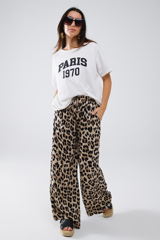 Model wearing Savanna Satin Pants in leopard print with a white Paris t-shirt and sunglasses for a stylish summer outfit.