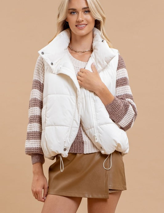 Woman wearing Dakota Quilted Puffer Vest in white with high collar and button closure, styled over a striped sweater and brown skirt.