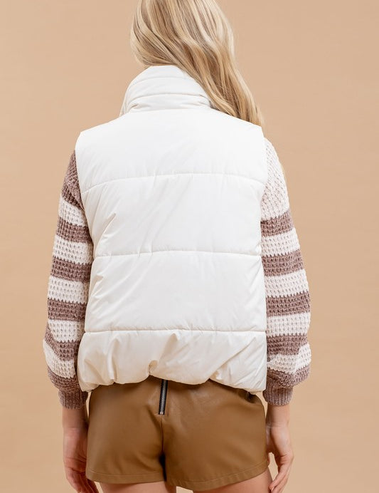 Woman wearing Dakota Quilted Puffer Vest with a high collar, styled over a striped sweater and shorts against a neutral background.