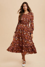 Woman wearing a Sarai Dress with abstract print, smocked bodice, puff sleeves, tiered skirt, blending elegance and comfort.