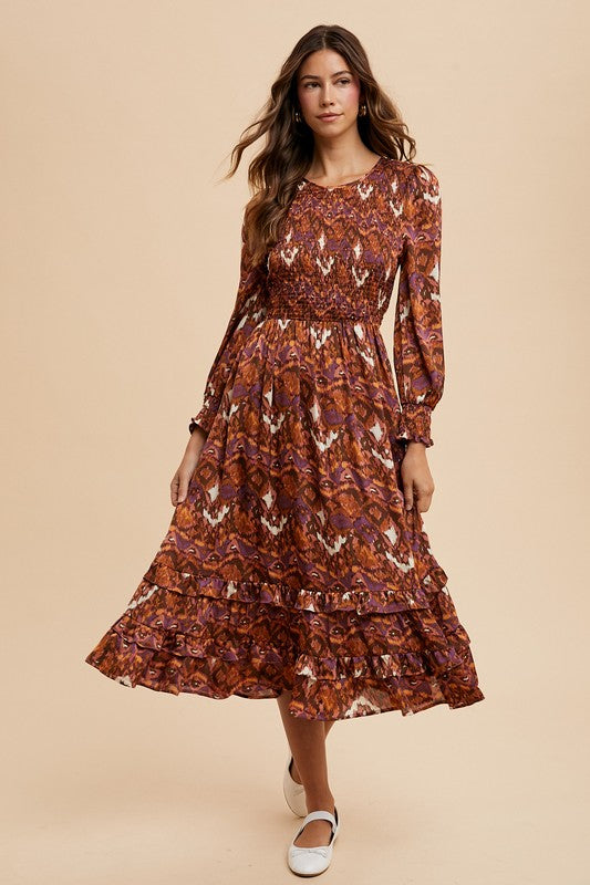 Woman wearing a Sarai Dress with abstract print, smocked bodice, puff sleeves, tiered skirt, blending elegance and comfort.