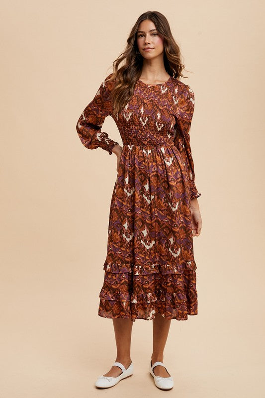 Woman wearing a Sarai Dress with abstract print, smocked bodice, long puff sleeves, and tiered skirt for an elegant day-to-night look.