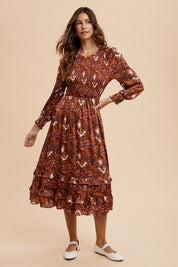 Woman modeling Sarai Dress with abstract print, smocked bodice, puff sleeves, and tiered skirt on woven fabric.