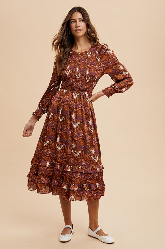 Woman modeling Sarai Dress with abstract print, smocked bodice, puff sleeves, and tiered skirt on woven fabric.