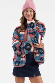 Woman wearing Sierra Tribal Shawl Jacket with vibrant print, high neck, and shawl collar, paired with a pink beanie and denim skirt.