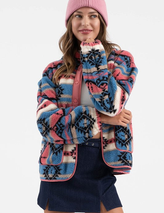 Woman wearing Sierra Tribal Shawl Jacket with vibrant print, high neck, and shawl collar, paired with a pink beanie and denim skirt.