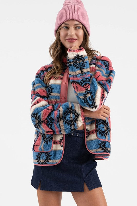 Woman wearing Sierra Tribal Shawl Jacket with vibrant print, high neck, and shawl collar, paired with a pink beanie and denim skirt.