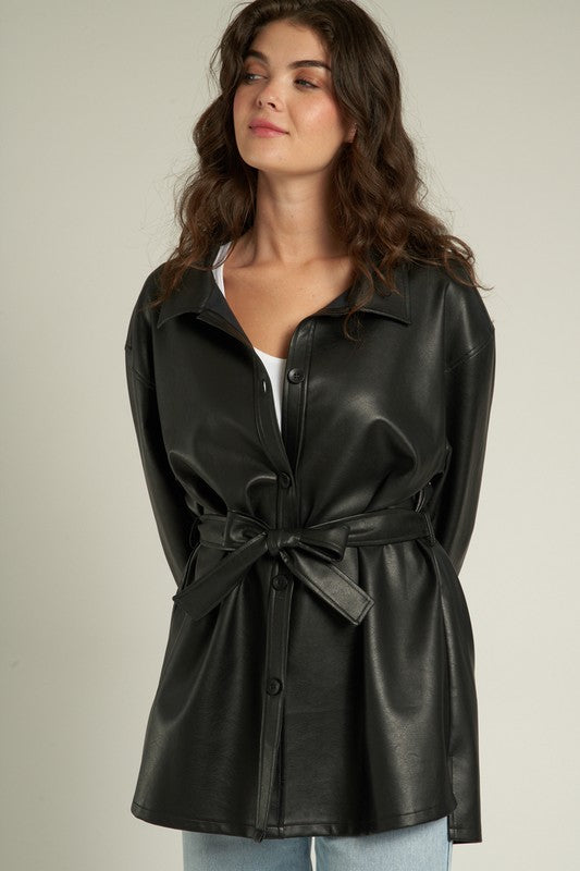 Woman modeling the Lyra Faux Leather Jacket, a trendy black shacket with a cinched waist and sleek finish.