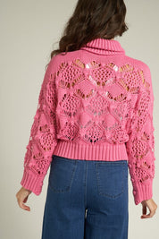 Woman wearing a pink Scarlette Crochet Sweater with intricate crochet design and a turtleneck, styled with high-waisted jeans.