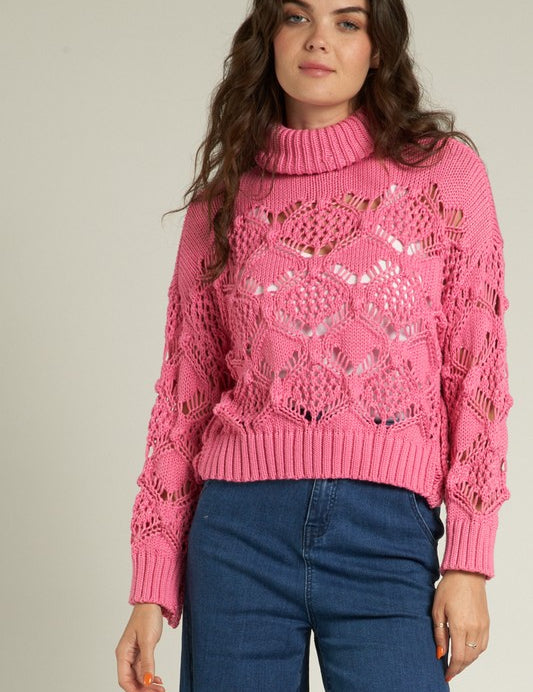 Cropped pink crochet sweater with turtleneck, styled for chic layering over jeans.