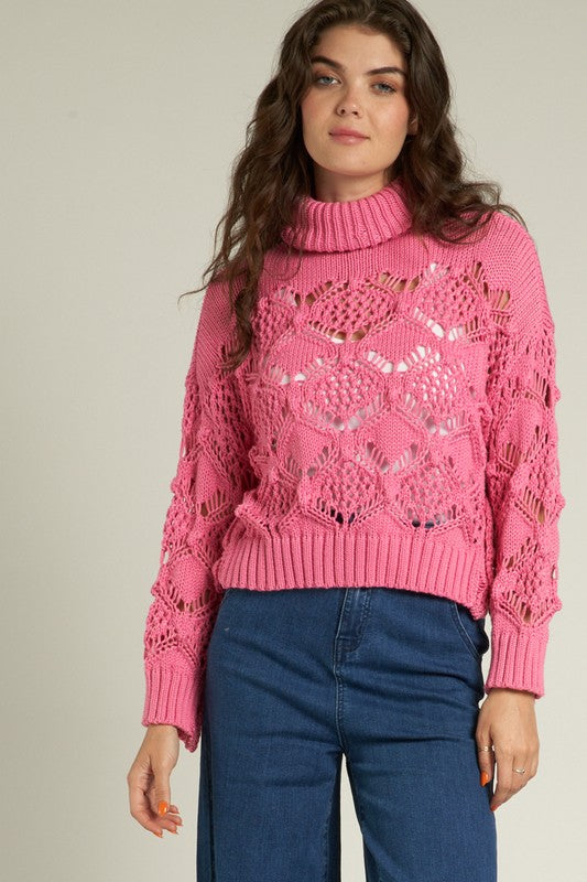 Cropped pink crochet sweater with turtleneck, styled for chic layering over jeans.