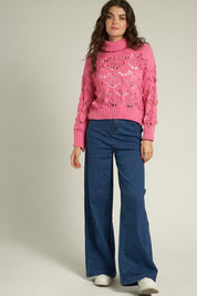 Model wearing a pink Scarlette Crochet Sweater with a turtleneck and wide-leg jeans, showcasing a chic casual style.