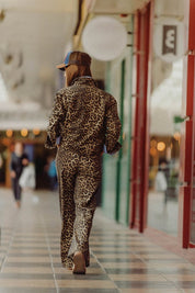 Woman walking in leopard print Lynx Denim Pants, showcasing a bold and chic street style in a shopping arcade.