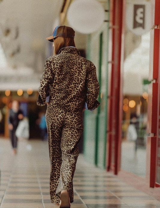 Woman walking in leopard print Lynx Denim Pants, showcasing a bold and chic street style in a shopping arcade.