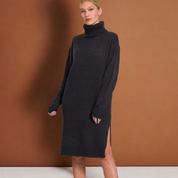 Woman wearing sable turtleneck sweater dress with long sleeves and side slit, standing against a brown background.