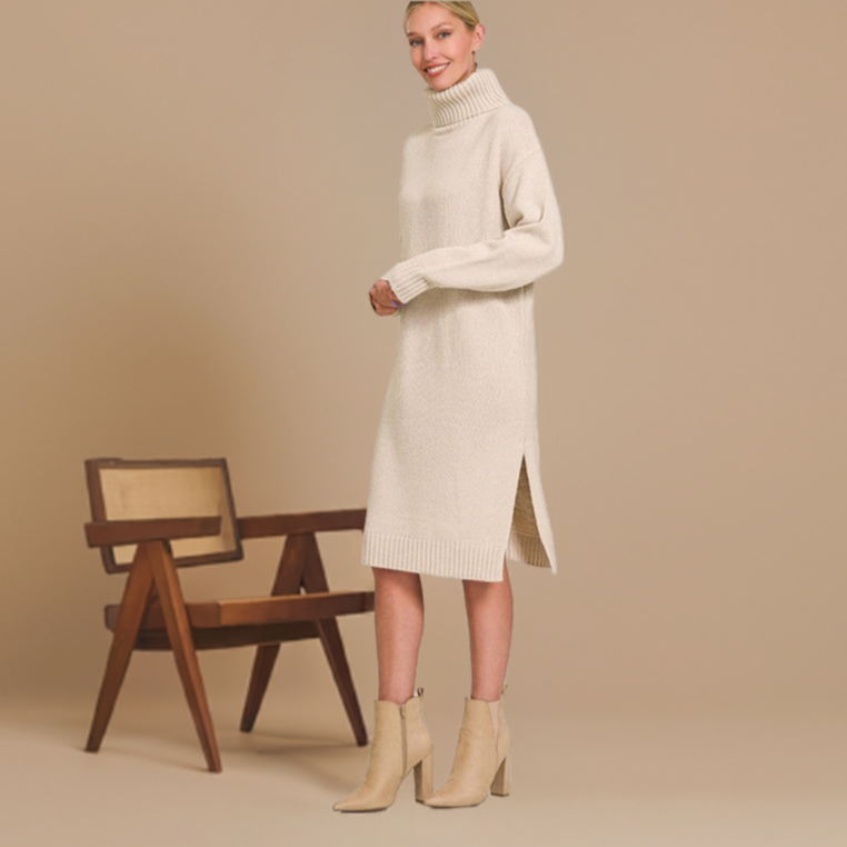 Woman wearing a sable turtleneck sweater dress with side slit, paired with tan ankle boots, standing beside a wooden chair.